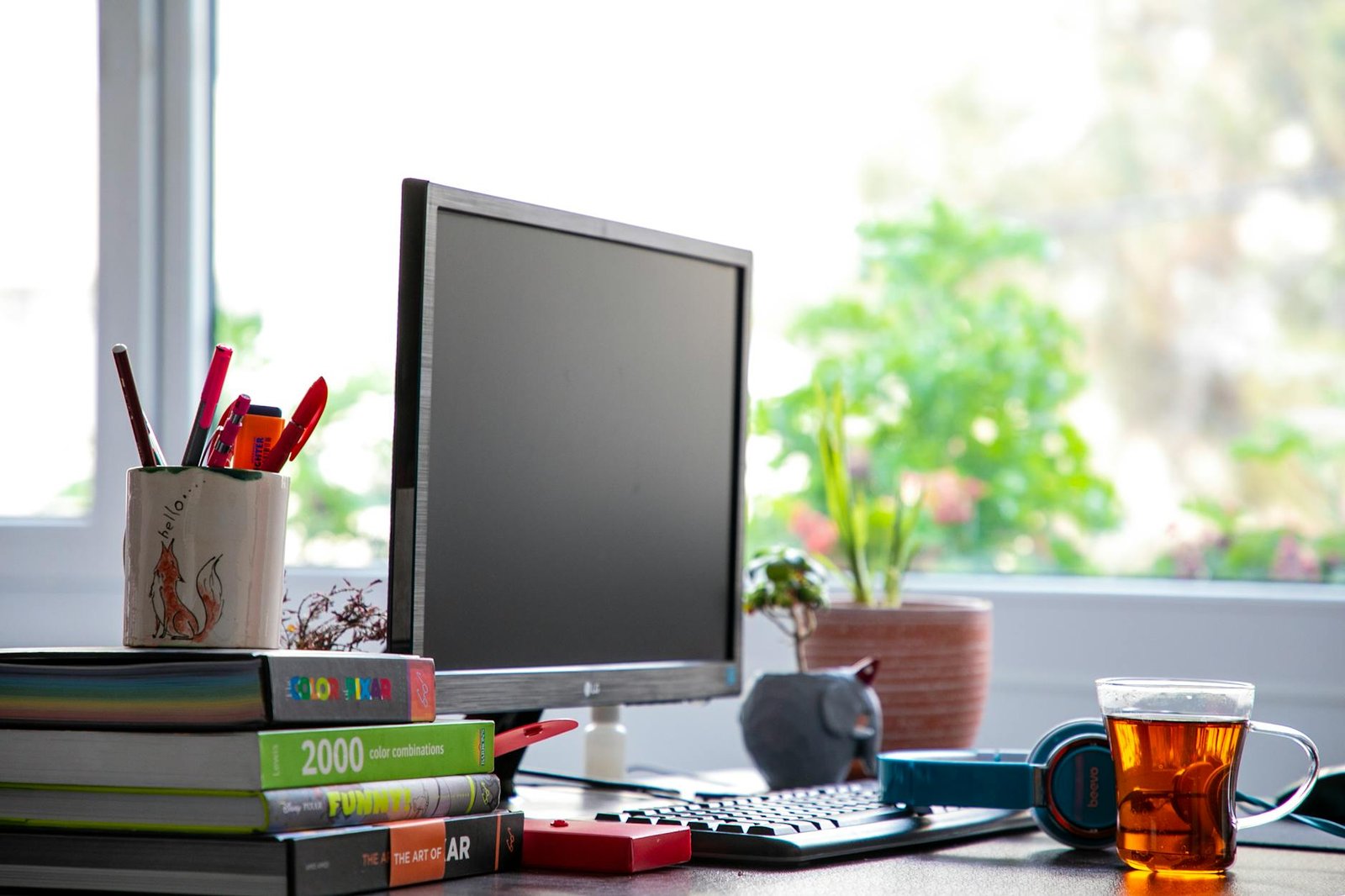 A steaming cup of tea sits on an office desk beside a laptop, notebooks, and a pen, suggesting a short break during work.
