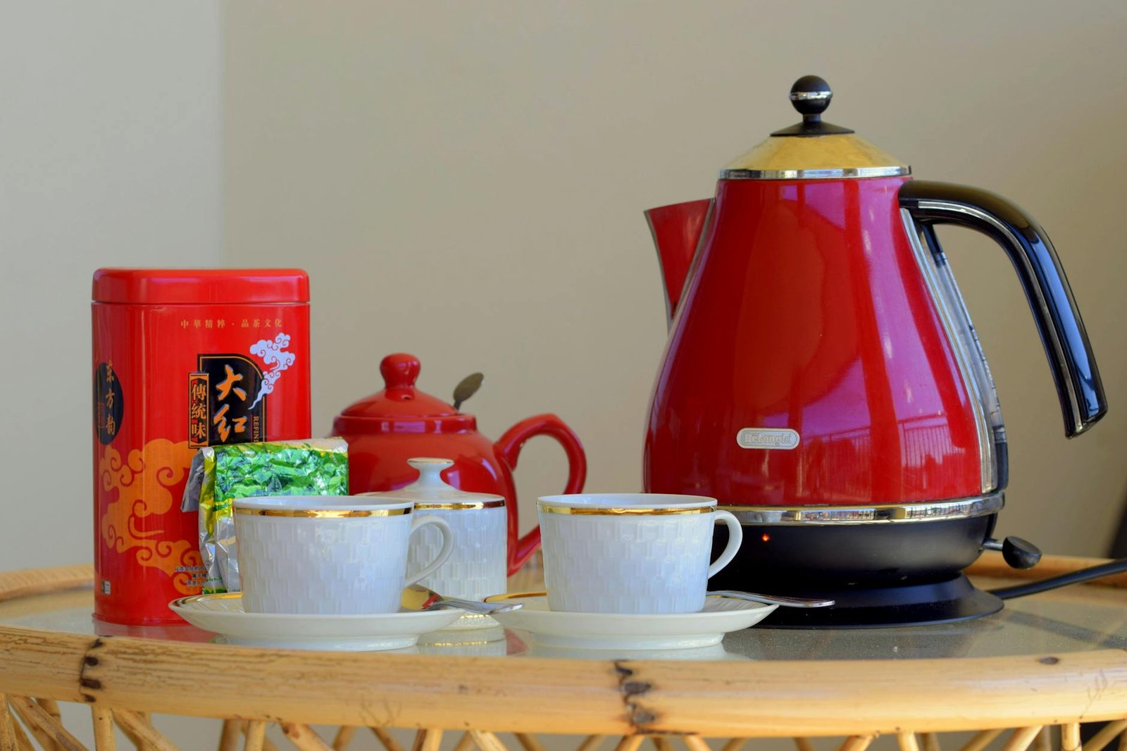 Red kettle on a table surrounded by ceramic mugs and labelled tea canisters, arranged as a tidy office tea station ready for use. Small accessories and a wooden surface create a welcoming communal break area.